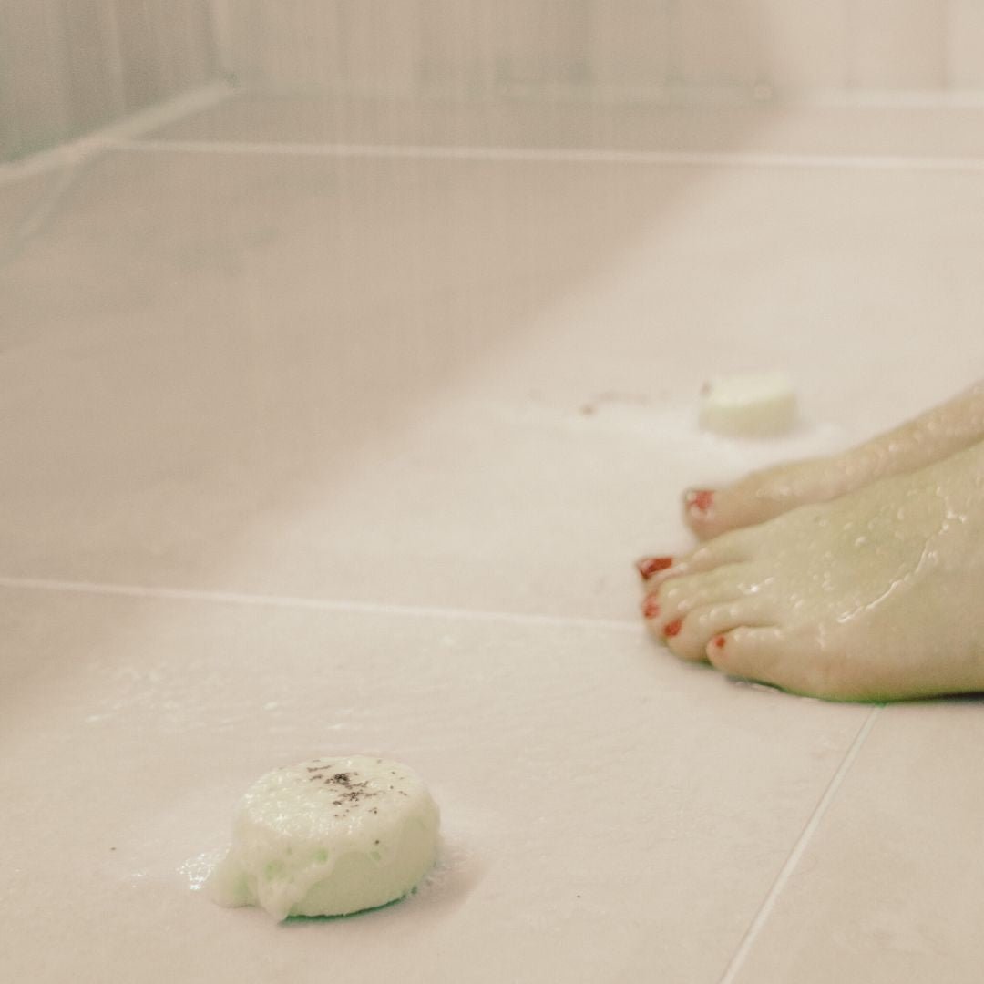 Lady using the 'Purity' shower steamer in the shower with refreshing Peppermint, Eucalyptus, and Ravensara essential oils, placed near her feet for an invigorating aromatherapy experience