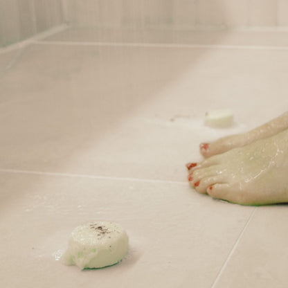 Lady using the 'Purity' shower steamer in the shower with refreshing Peppermint, Eucalyptus, and Ravensara essential oils, placed near her feet for an invigorating aromatherapy experience