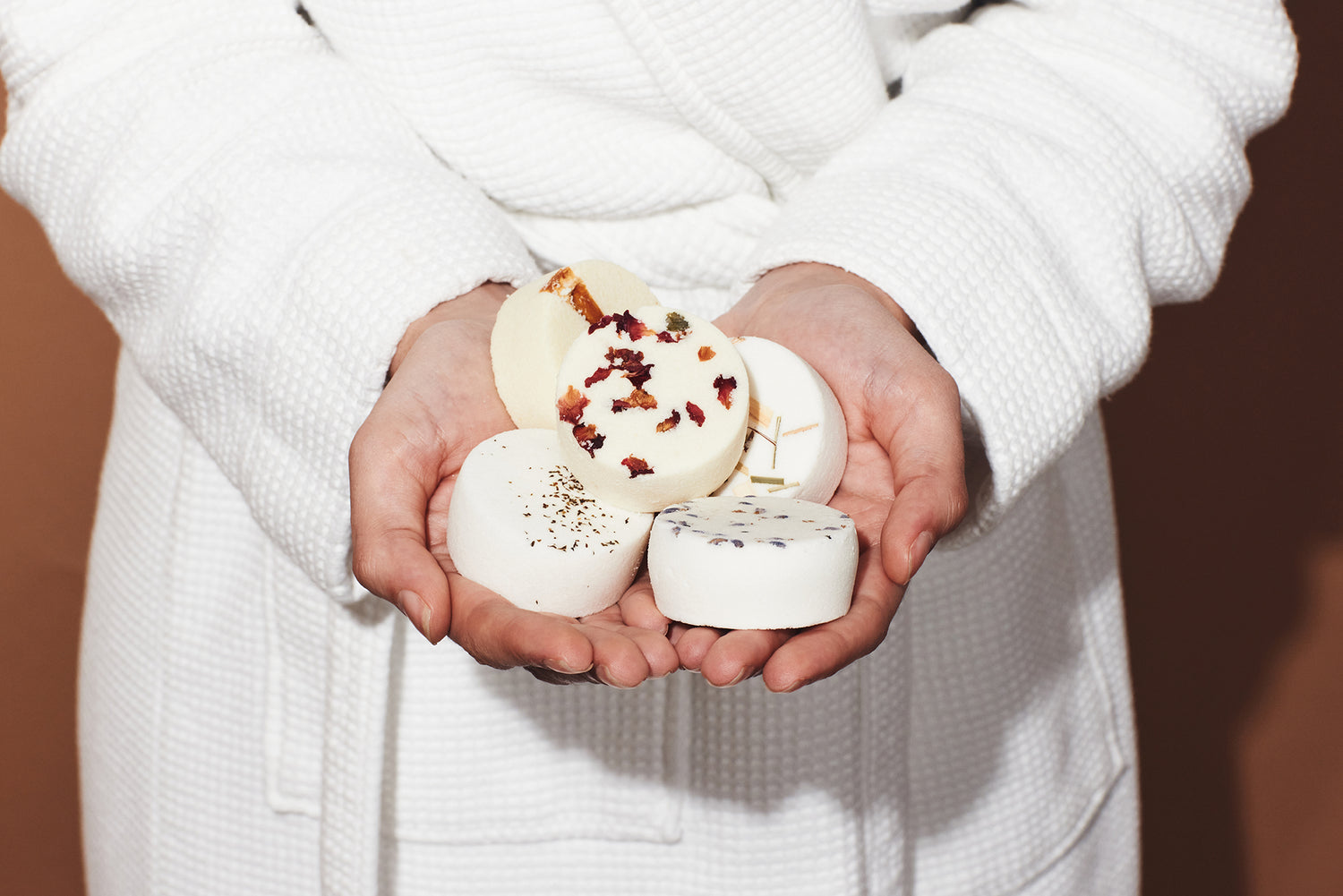 Person holding five aromatherapy shower steamers with botanicals in a white robe.