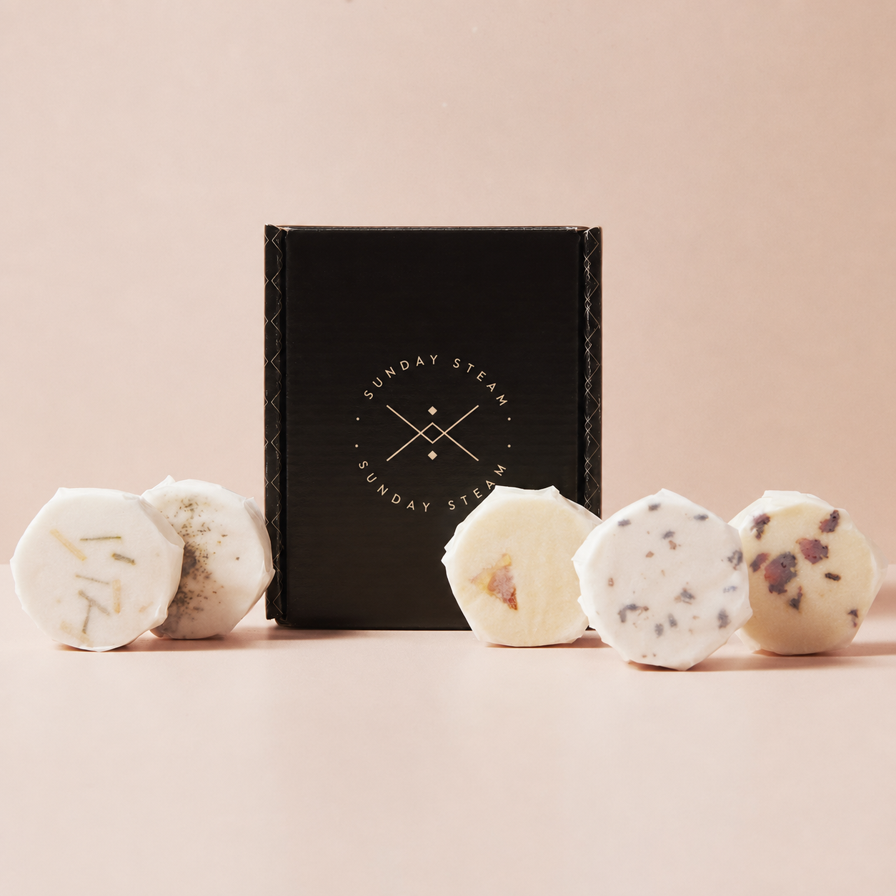 Sunday Steam aromatherapy shower steamers displayed around a black gift box on a soft pink background.