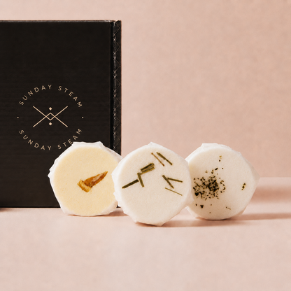 Sunday Steam Energise & Refresh shower steamers with citrus, rosemary and botanical toppings displayed in front of a black gift box.