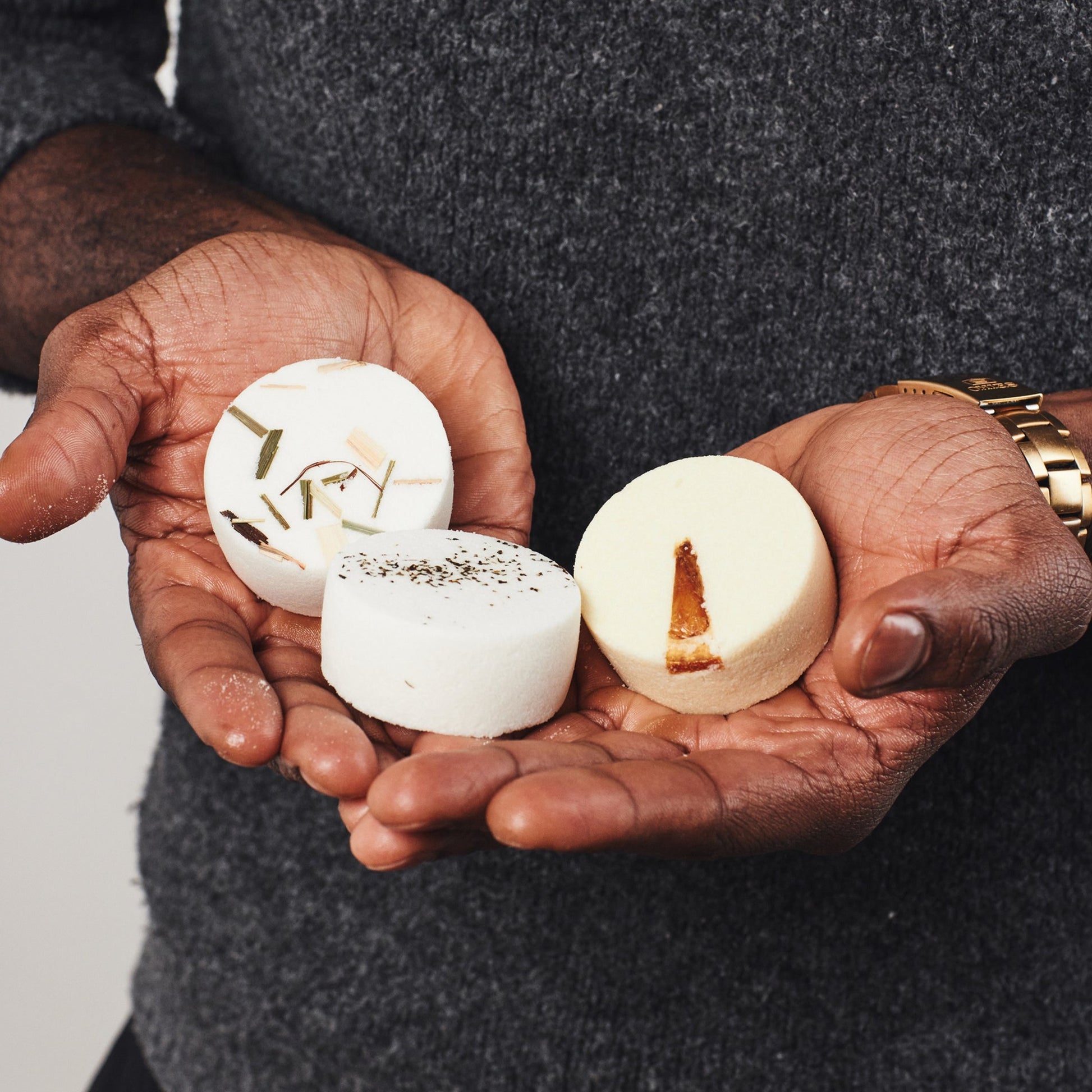 Three Sunday Steam aromatherapy shower steamers with botanical toppings held in cupped hands.